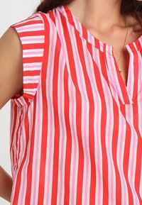 Punavalkoraidallinen pusero, jossa on kap-skaftimet, V-aukko ja kevyt kangastuntuma. Pystysuorat raidat vaihtelevilla leveyksillä.