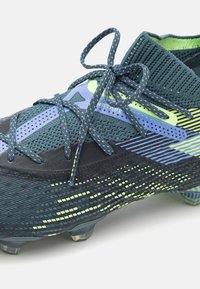 Scarpino da calcio di colore blu scuro e nero con parte superiore testurizzata, dettagli verde e blu, colletto in maglia e tacchetti in gomma per la presa.