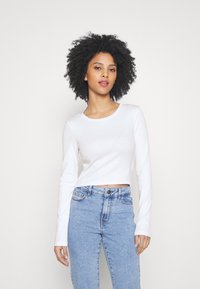 White long-sleeve cropped top with a round neck and ribbed texture, paired with blue high-waisted jeans featuring a classic button closure.