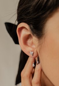Pendientes colgantes de plata con un diseño floral, un eslabón de cadena y una piedra en forma de lágrima al final, con una textura pulida.