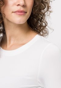 Camicia bianca attillata con collo a giro, realizzata in tessuto morbido. Texture soffice con maniche corte e dettagli di cucitura sottili.
