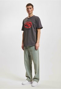 Grå T-skjorte med rødt logo, løs passform. Sammen med lysegrønne baggy jeans og hvite joggesko. Enkelt design, bomullsmateriale.