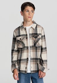 Męska koszula flanelowa w kremowym kolorze w brązowo-czarną kratę, z guzikami z przodu, dwiema kieszeniami na piersiach i miękką teksturą. Połączona z białym T-shirtem.