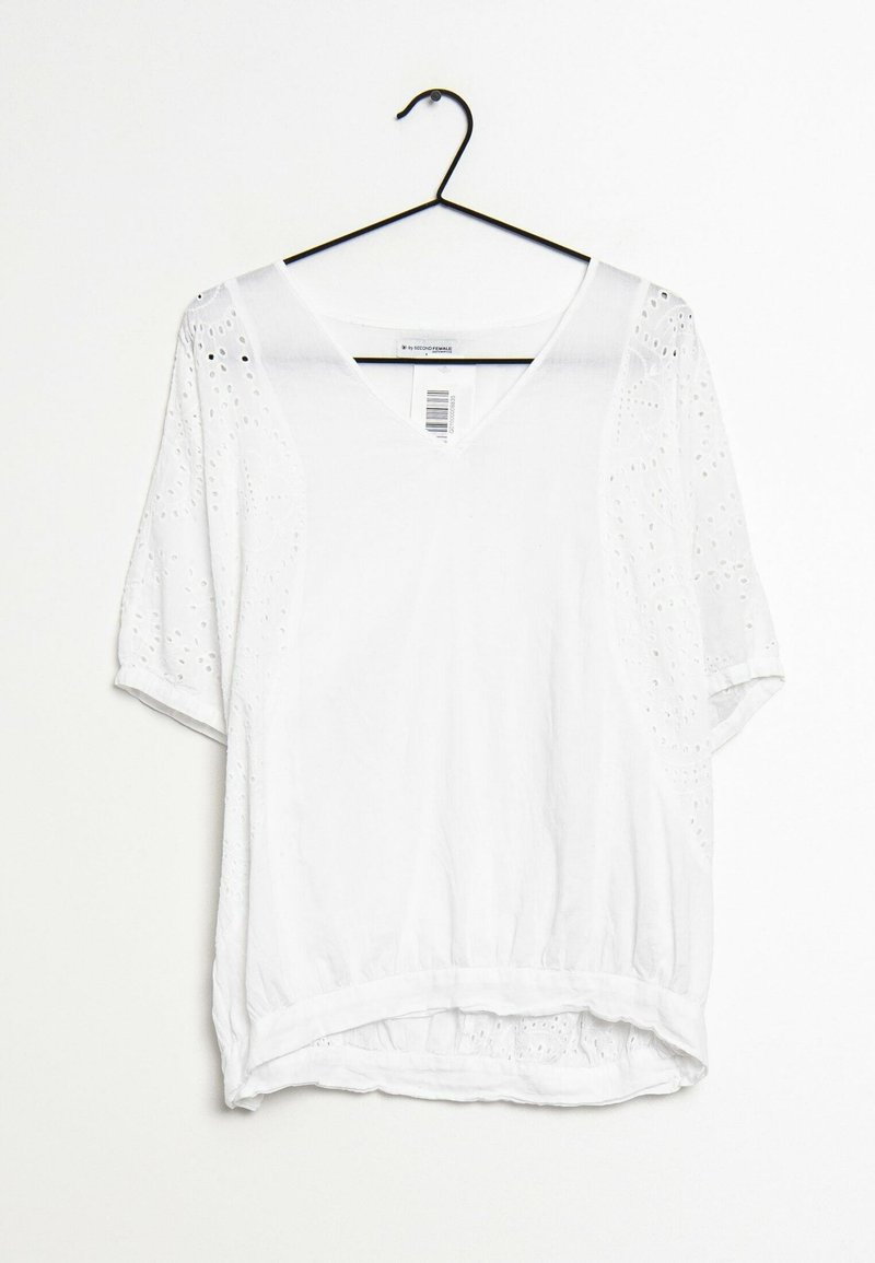 Blouse blanche à manches courtes avec un col en V, ornée de détails en œillets sur les manches et un ourlet froncé. Tissu léger, design décontracté.