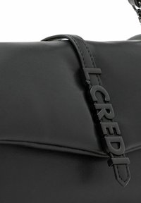 Bolso de mano de cuero negro con una textura suave, una forma estructurada y un logotipo embosado prominente como detalle destacado.