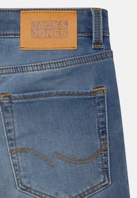 Zadní kapsa modrých džín s oranžovým prošíváním a hnědým koženým štítkem s nápisem Jack & Jones na pase.