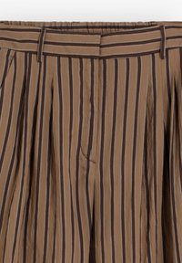 Bruine katoenen broek met verticale zwarte en witte strepen en plooien, voorzien van een tailleband met riemlussen.