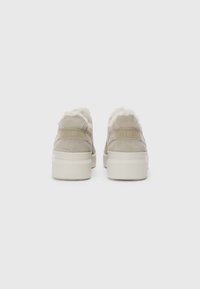 Beige nubukist sneakers, mille pehme valge karvast vooder kaela ümber, lame valge kummitald ja väike logo detail kandadel.