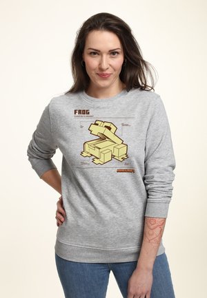 Szara bluza z żółtą grafiką żaby z Minecrafta, zawierająca szczegóły techniczne, z ściągaczami przy mankietach i u dołu. Model nosi niebieskie dżinsy.