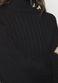 Svart ribbad polotröja med långa ärmar. Tillverkad av stickat tyg, med hög nacke och en texturerad yta.