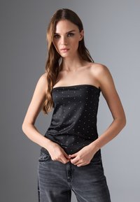 Top negro sin mangas con pequeños lunares blancos, hecho de una tela suave. La modelo lo lleva con unos jeans gris oscuro. Diseño simple y ajustado.