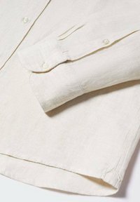 Vaaleanbeige pellavapaita, jossa on napitettava kaulus, pitkät hihat ja pyöristetty helma. Etutasku napituksella.