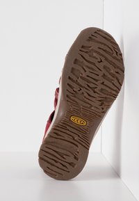 Sola di scarpa rossa e marrone con un motivo testurizzato e logo di marca. Il materiale in gomma offre aderenza con scanalature profonde per una maggiore trazione.
