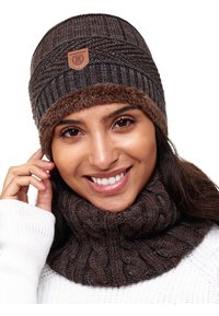 Knitted brown beanie with a textured design and faux fur lining, featuring a leather logo patch. Matching brown cowl with cable knit pattern.