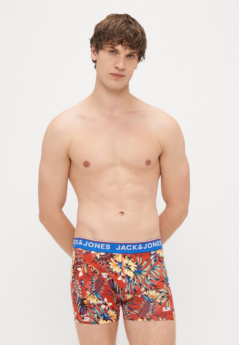 Red boxer shorts with a blue waistband featuring "JACK & JONES" logo. The fabric displays a vibrant tropical pattern of flowers and leaves.