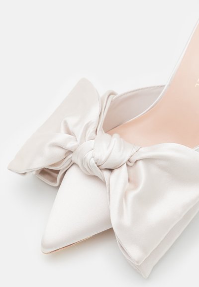 Pointed-toe high heel with a satin texture, featuring a large bow detail at the front. Color is pale beige, with a smooth finish.