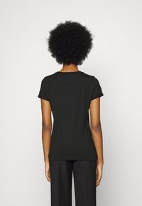 Schwarzes Baumwoll-T-Shirt mit kurzen Ärmeln, Rundhalsausschnitt und taillierter Silhouette, von hinten betrachtet. Glatte Textur und minimalistisches Design.