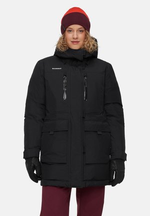 Zwarte geïsoleerde parka met een capuchon, voorzien van twee met rits afsluitbare zakken en een logo op de borst. Draagt een rode en paarse muts en zwarte handschoenen.