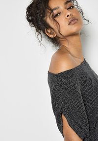 Czarna bluzka typu off-the-shoulder z fakturowanym wzorem z srebrnych nici. Ma krótkie rękawy i luźny krój. Wykonana z miękkiego materiału o lekkim połysku.