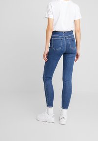 Úzké modré džíny s vysokým pasem, vyrobené z denimu. Mezi vlastnosti patří dvě zadní kapsy a decentně brandovaná nášivka na pasu.