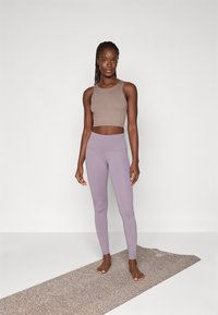 Brown crop top and light purple leggings, fitted design, stretchy fabric, minimalistic style, standing on a textured yoga mat.