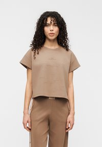 Καφέ κοντομάνικη cropped μπλούζα με ανάγλυφα κείμενα στο ύφασμα. Το ύφασμα είναι λείο, με άνετη εφαρμογή και στρογγυλή λαιμόκοψη.
