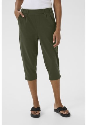 Pantalons capri vert olive avec une texture lisse, dotés de poches avant, d'une taille large et d'un design au niveau des chevilles. Associés à des sandales noires.