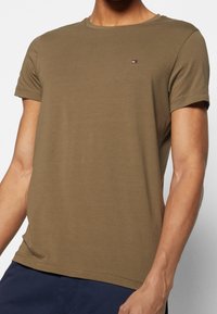 Oliivinvihreä lyhythihainen T-paita pehmeästä kankaasta, pyöreällä pääntiellä ja pienellä logoyksityiskohdalla rinnassa. Sileä pinta ja rento istuvuus.