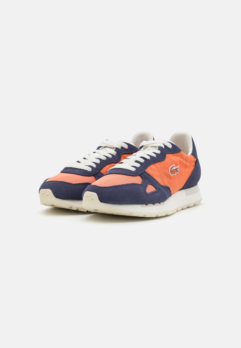 Un par de zapatillas naranja y azul marino con cordones blancos, suelas blancas y un pequeño logo de cocodrilo en el lateral.