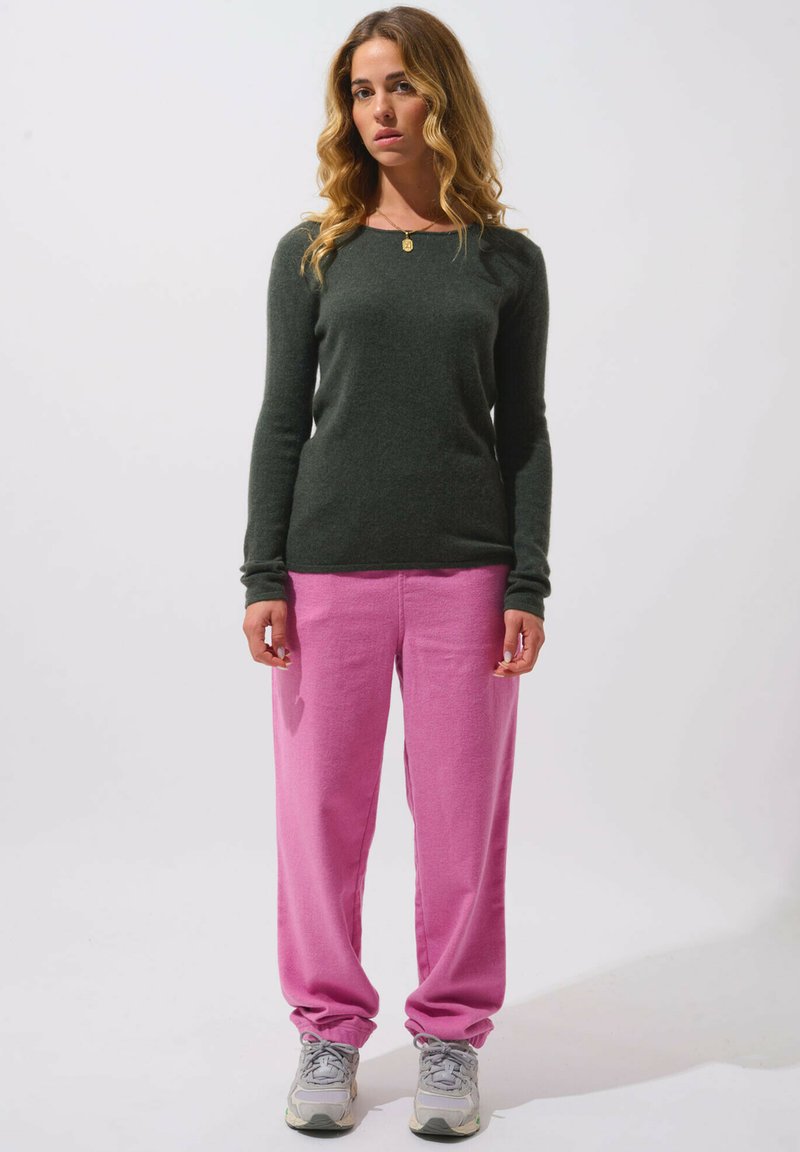 Maglione a maniche lunghe verde scuro abbinato a pantaloni della tuta rosa chiaro. I pantaloni presentano una vestibilità rilassata, cuciture dettagliate e polsini elasticizzati.
