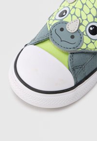 Πράσινο και γκρι αθλητικό παπούτσι με σχέδιο δεινόσαυρου, με λαστιχένιο λευκό καπάκι στα δάχτυλα, μαλακό ύφασμα και ιμάντα με βέλκρο για κλείσιμο.