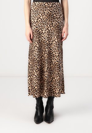 Femme portant une jupe midi à imprimé léopard associée à des bottines noires à bout pointu, debout devant un fond blanc uni.