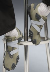 Oliwkowe sneakersy z szarymi akcentami, wykonane z teksturowanej tkaniny, z dwoma elastycznymi paskami oraz solidną czarną podeszwą z kolcami.