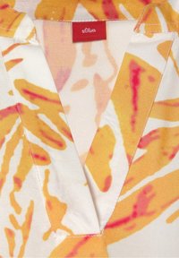 Blouse à manches courtes avec col en V, présentant une base blanche avec des motifs abstraits jaunes et roses, fabriquée en tissu léger.