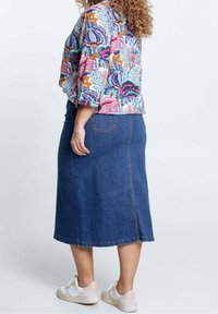 Jupe en denim à coupe droite avec poches arrière, associée à un haut à motifs floraux colorés. Le haut a des manches trois-quarts.