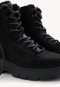 Stivaletti neri in suede con superficie testurizzata, dotati di lacci neri tondi e una suola robusta. Includono finiture in metallo nero.