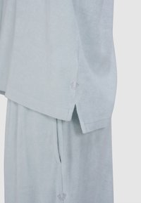 Lichtblauw loungewear set gemaakt van zachte stof. De top heeft een comfortabele pasvorm met zijsplitten; de onderkant heeft zakken en een geborduurd logo.
