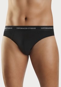 Svarte bomullstruser med en tettsittende design, med en bred elastisk linning merket "COPENHAGEN STUDIOS" i hvitt, glatt tekstur.