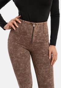 Pantaloni alti in vita, di colore marrone, con una chiusura centrale con zip e tasche laterali, caratterizzati da un leggero motivo marmorizzato e una finitura in tessuto liscia.