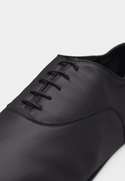 Κοντινή λήψη ενός μαύρου δερμάτινου παπουτ σιού φόρεμα με κλειστό κορδόνι και καθαρή ραφή σε λευκό φόντο.