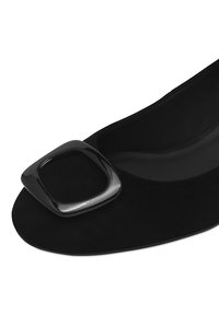 Chaussure plate en suède noir avec un détail de boucle carrée en noir brillant sur le bout. Doublure intérieure lisse et design à bout arrondi.