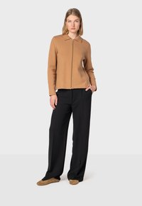 Brun zip-up sweater med krave, båret med højtaljede sorte brede bukser og lysebrune flade sko. Glat tekstur, afslappet design.