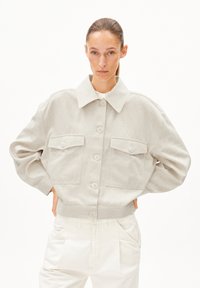 Hellgraue, kurze Jacke aus strukturiertem Stoff mit großem Kragen, Knopfverschluss und zwei Taschen mit Klappen auf der Brust.