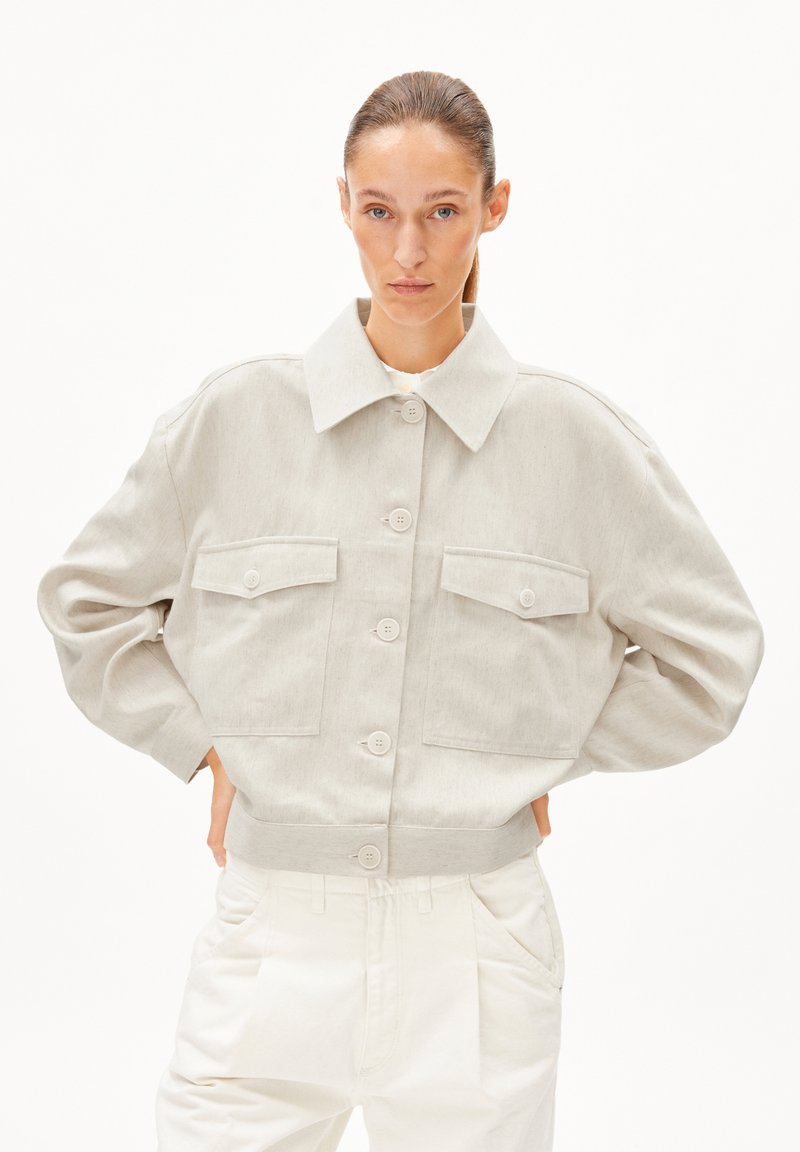 Hellgraue, kurze Jacke aus strukturiertem Stoff mit großem Kragen, Knopfverschluss und zwei Taschen mit Klappen auf der Brust.