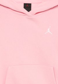 Sudadera rosa claro con un bolsillo frontal y el logo Jumpman blanco en el pecho, mostrando la capucha y la etiqueta negra de la marca Jordan en el interior del cuello.