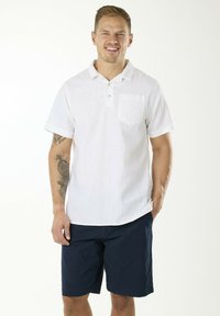 Weißes Kurzarmhemd mit Kragen und Brusttasche, kombiniert mit navy Shorts. Weicher Stoff, lässiges Design und hochgerollte Ärmelabschlüsse.