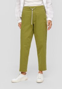 Pantalons en coton mélangé verts avec une taille élastique, longueur cheville, poches latérales et texture lisse, associés à des baskets blanches.