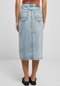 Denim midiskjørt i lyseblått, med høy livlinje, to baklommer og en rett silhuett. Brukt med svarte platåsandaler.