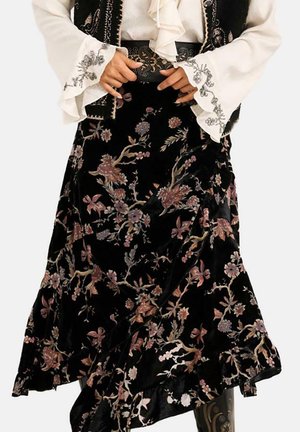 Persona que lleva una falda negra con estampado floral, un cinturón ancho bordado y una blusa blanca con mangas con volantes.