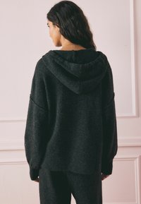 Übergroßer schwarzer Kapuzenpullover aus weichem Strickstoff. Mit weiten Ärmeln und geripptem Saum. Rückansicht, die die lockere Passform und Textur zeigt.